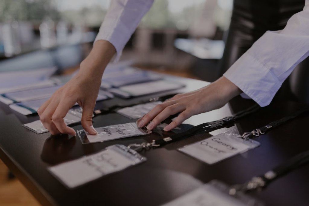 Corporate event staffing team member arranging name badges and lanyards at a conference registration desk, preparing for guest check-in.